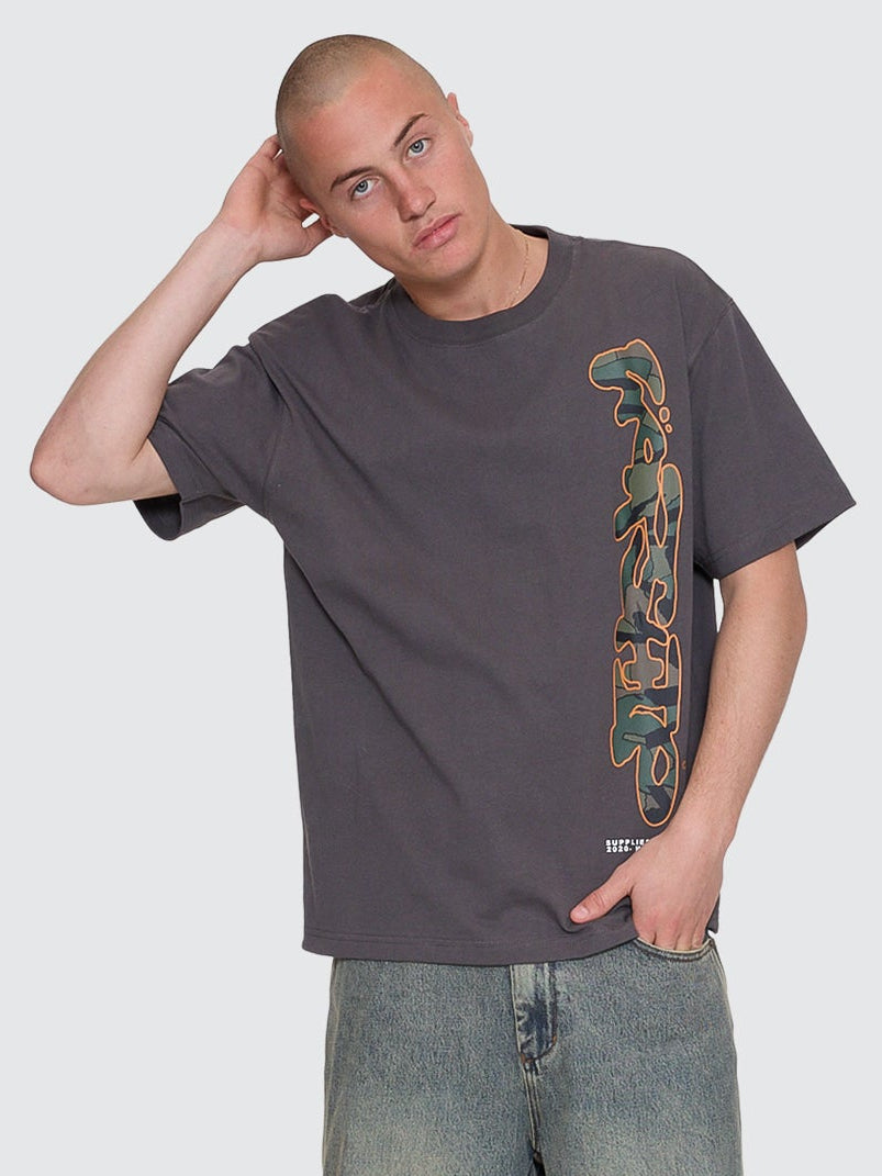 Person wearing a dark gray t-shirt with a graphic design and denim shorts on a white background